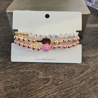 A set of three beaded stretch bracelets. The bracelets feature rose gold metallic beads, white letter beads spelling 'PICKLEBA', and a pink polka dot charm.