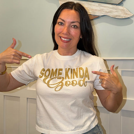 Jess wearing a white t-shirt with 'SOME KINDA Good' in gold letters, pointing at the text.